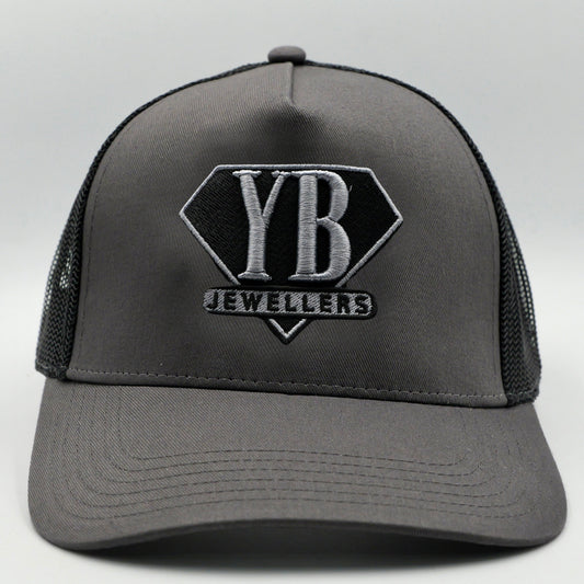 Gray trucker cap with black mesh and YB Jewelers logo on a light gray background