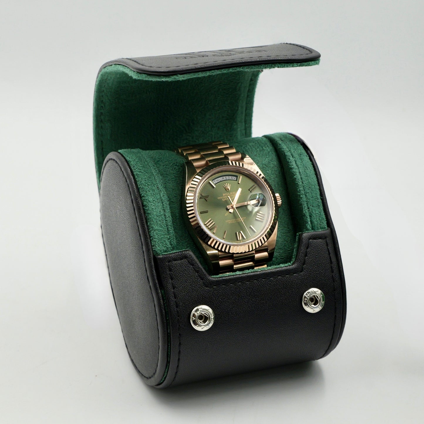Gold watch in a green and black watch case on a white background