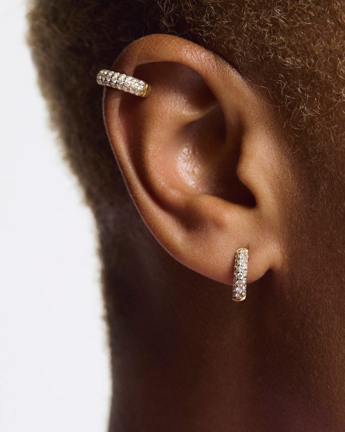 Close-up of an ear wearing two diamond stud earrings with a blurred background pair of huggiee earrings in 18k white gold platinum with micro diamond setting by yb jewellers