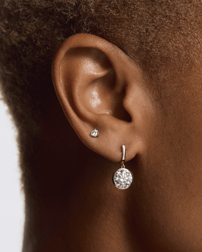 Close-up of an ear wearing a diamond earring with a plain background yb jewellers yellow gold diamond drop earrings rubover setting