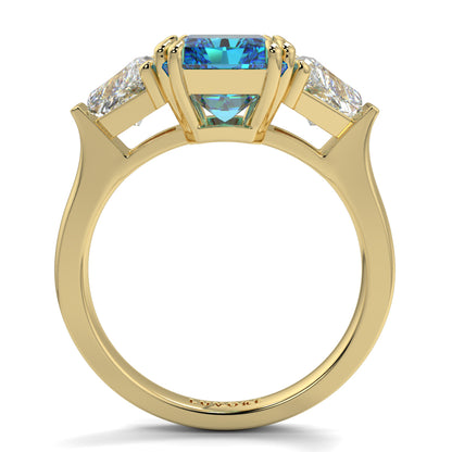 Gold ring with a blue gemstone and diamond accents on a white background Introducing daisy radient square blue lab grown diamond engagement ring set in yellow gold with lab grown side diamonds 18k yellow gold coloured diamond ring 
