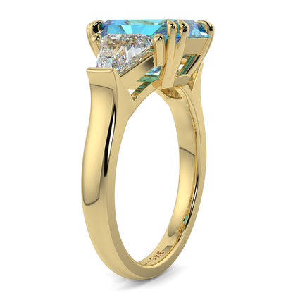 Gold ring with a blue gemstone and diamond on a white background Introducing daisy radient square blue lab grown diamond engagement ring set in yellow gold with lab grown side diamonds 18k yellow gold coloured diamond ring 