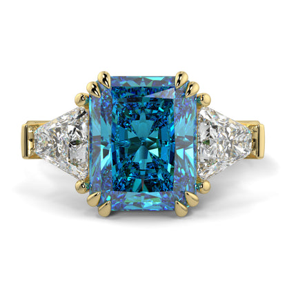 Ring with a blue gemstone and gold accents on a white background Introducing daisy radient square blue lab grown diamond engagement ring set in yellow gold with lab grown side diamonds 18k yellow gold coloured diamond ring 