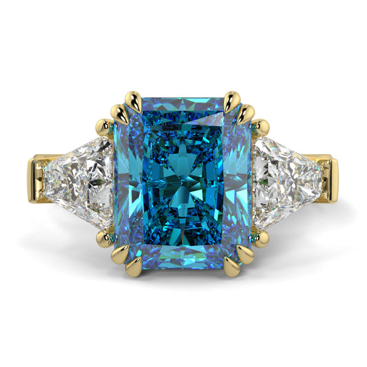 Ring with a blue gemstone and gold accents on a white background Introducing daisy radient square blue lab grown diamond engagement ring set in yellow gold with lab grown side diamonds 18k yellow gold coloured diamond ring 