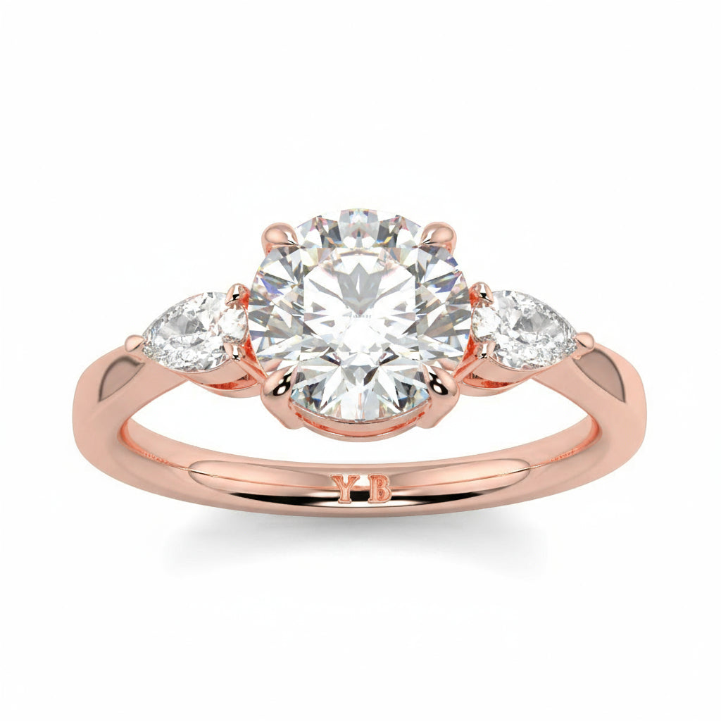 Rose gold ring with a large diamond and smaller diamonds on the sides against a white background yb jewellers 3 stone trilogy engagement ring round and pear shape best selling design trending diamond ring