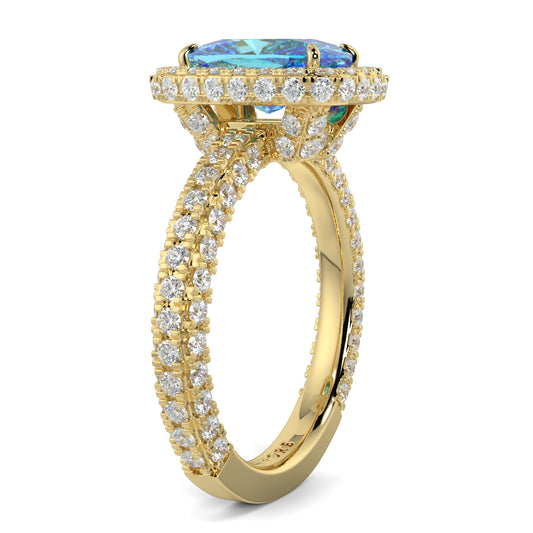 Gold ring with a blue gemstone and diamond accents on a white background yb jewellers cushion blue diamond engagement ring in a halo diamond ring lab grown with diamond encrusted hidden halo and band