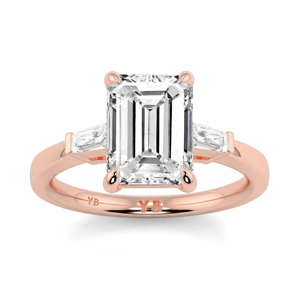 Rose gold ring with a large emerald-cut diamond and smaller diamonds on a white background yb_jewellers_3_stone_trilogy_engagement_ring_round_and_pear_shape_best_selling_design_trending_diamond_ring