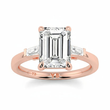 Rose gold ring with a large emerald-cut diamond and smaller diamonds on a white background yb_jewellers_3_stone_trilogy_engagement_ring_round_and_pear_shape_best_selling_design_trending_diamond_ring