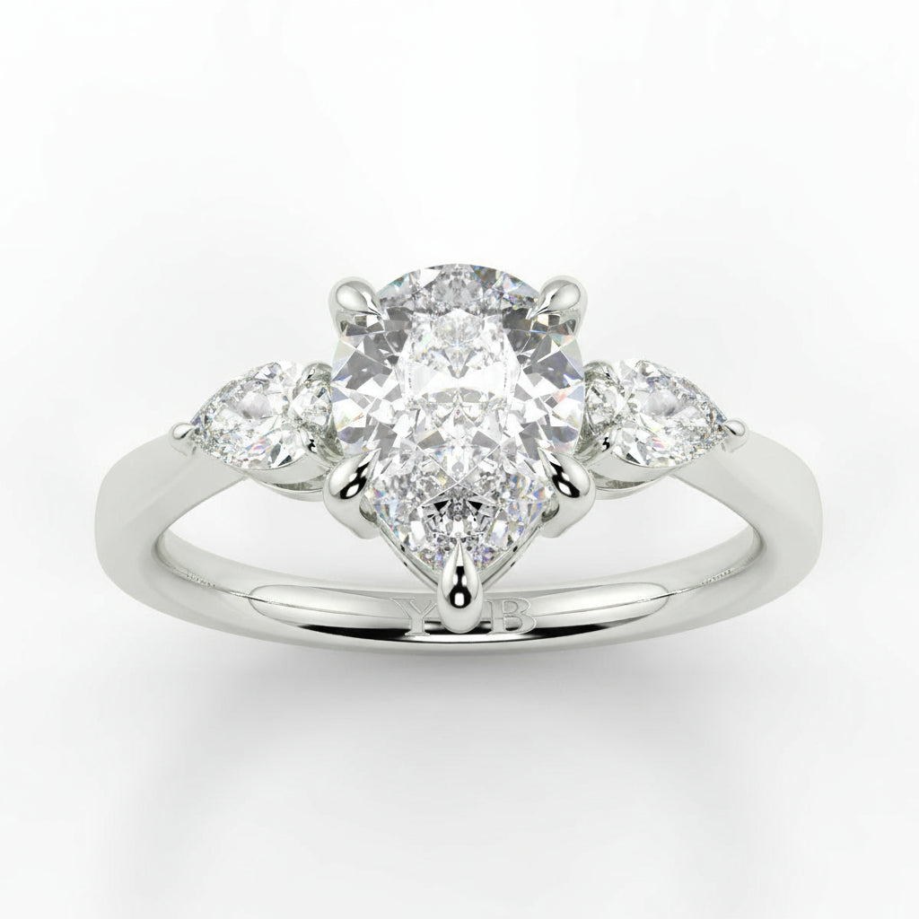 Diamond ring with a central pear-shaped diamond and two smaller diamonds on a white background _yb_jewellers_3_stone_trilogy_engagement_ring_round_and_pear_shape_best_selling_design_trending_diamond_ring