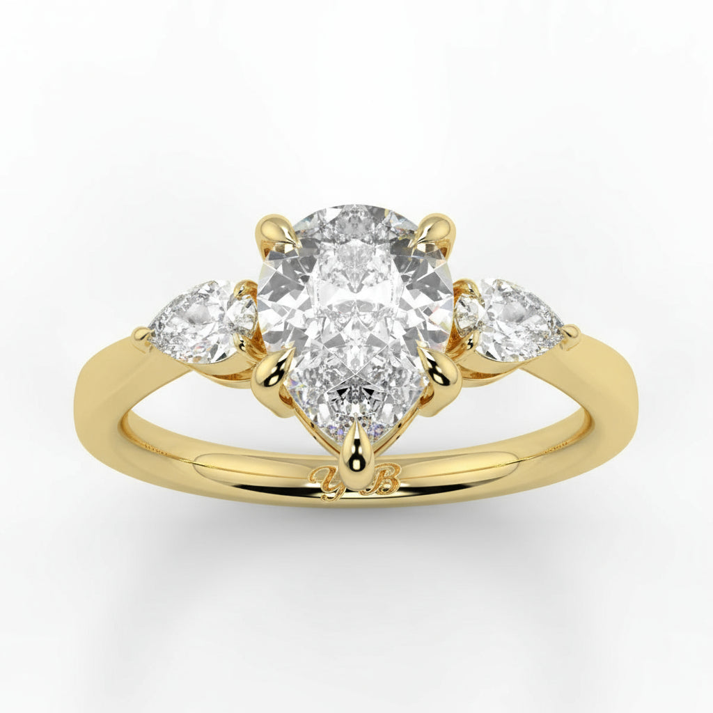 Gold ring with a central pear-shaped diamond and two side stones on a white background _yb_jewellers_3_stone_trilogy_engagement_ring_round_and_pear_shape_best_selling_design_trending_diamond_ring