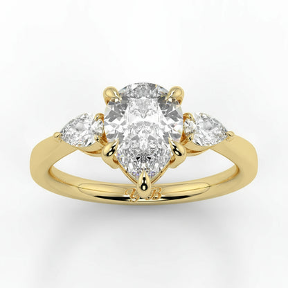 Gold ring with a central pear-shaped diamond and two side stones on a white background _yb_jewellers_3_stone_trilogy_engagement_ring_round_and_pear_shape_best_selling_design_trending_diamond_ring