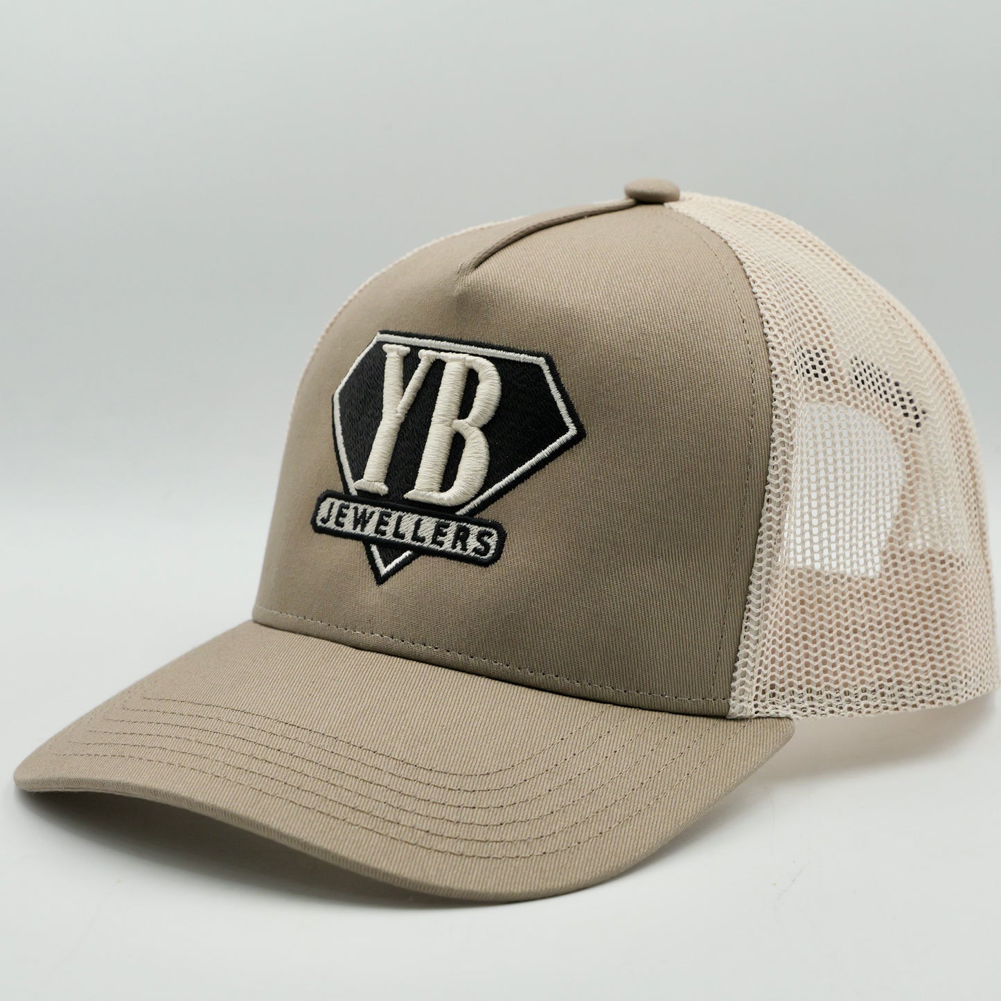 Beige trucker cap with 'YB Jewellers' logo on a light gray background