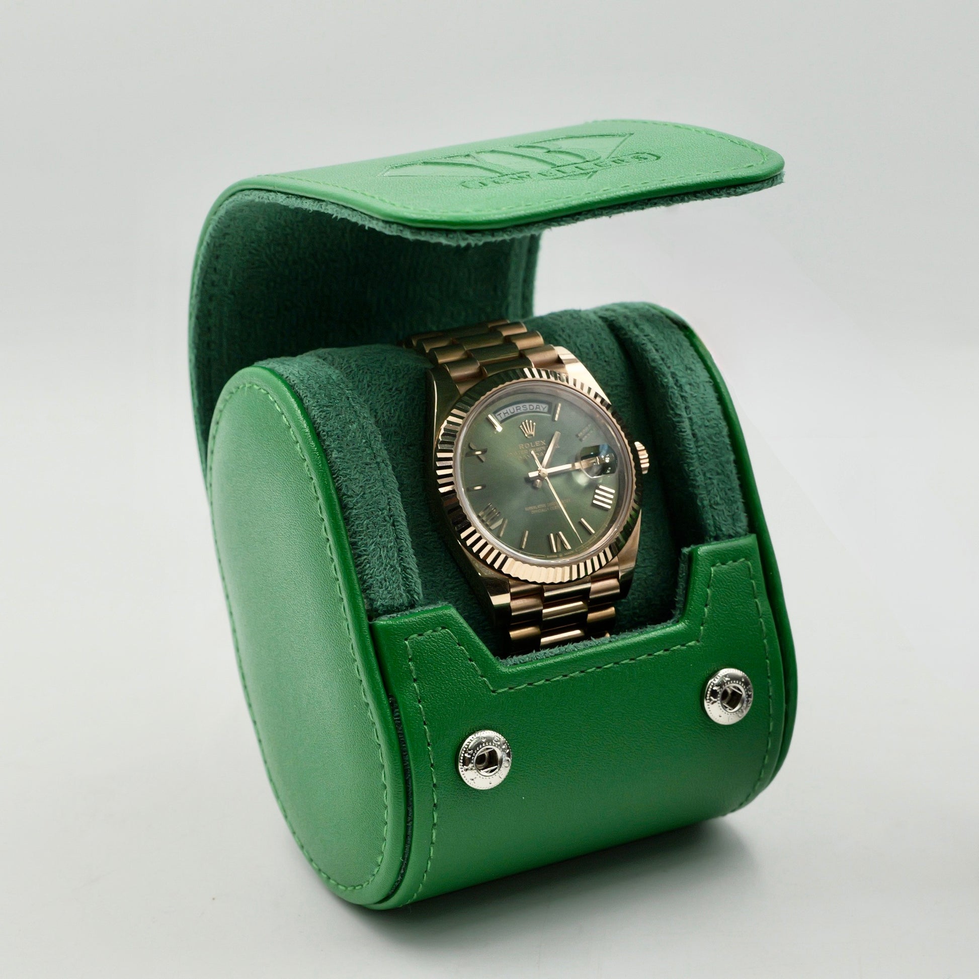 Green watch box with a gold watch inside on a gray background