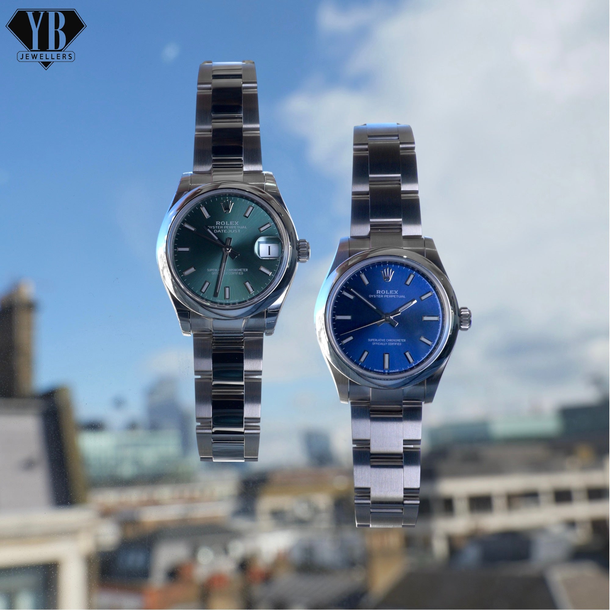Two silver watches with green and blue faces on a blurred cityscape background
