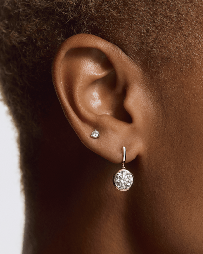Close-up of an ear wearing a diamond earring with a plain background  yb jewellers yellow gold diamond drop earrings rubover setting